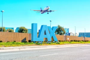 An aircraft flying over the LAX sign at Los Angeles airport.
