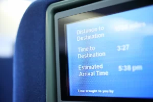 A monitor on a seat in an aircraft displaying information about the time and distance to the final destination.